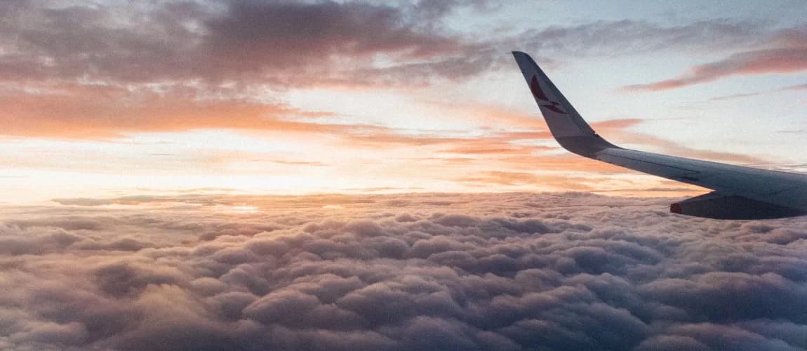 Ein Flugzeug im Himmel, im Hintergrund ist ein Sonnenaufgang.