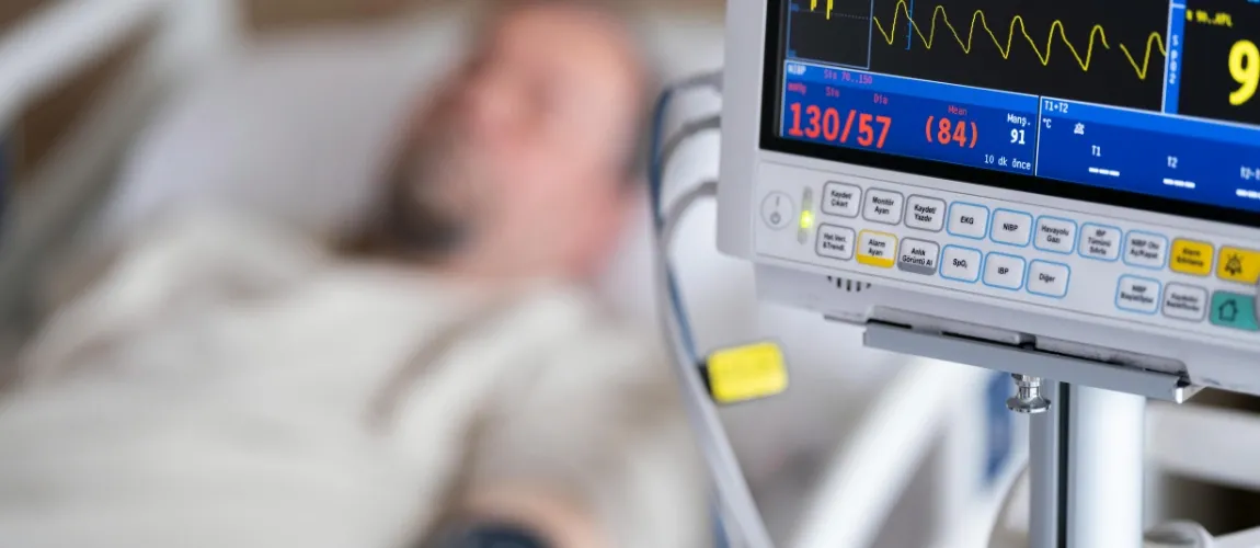 Fokus auf eine medizinische Überwachungseinheit, im Hintergrund liegt ein Patient im Bett.