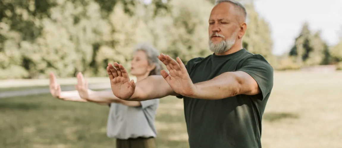 Eine Frau und ein Mann strecken auf einer Wiese stehend die Arme nach vorne aus.