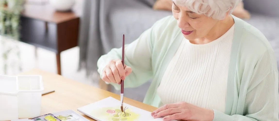 Eine Seniorin malt mit einem Pinsel ein Bild.