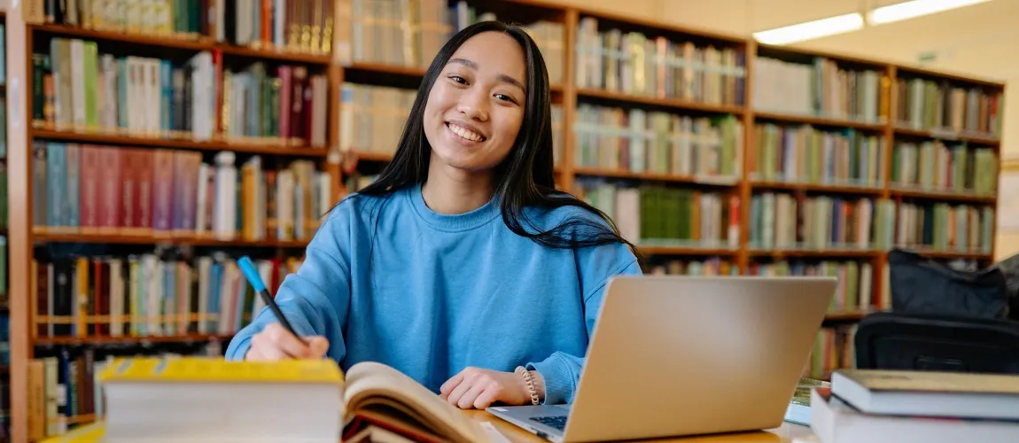 Eine dunkelhaarige Frau sitzt an einem Schreibtisch und lächelt in die Kamera.