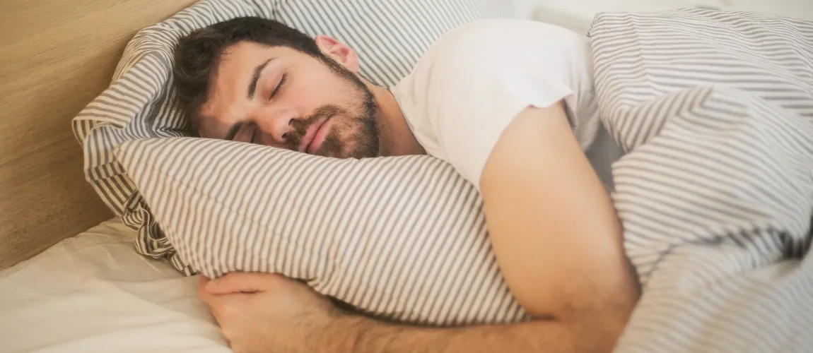 Ein Mann liegt schlafend inmitten eines gestreiften Bettzeugs. 