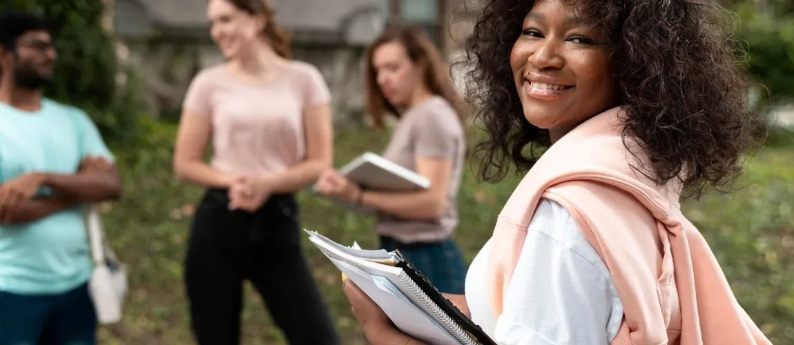 Eine Frau steht mit Unterlagen im Vordergrund und blickt lächelnd in die Kamera, dahinter stehen mehrere Personen.