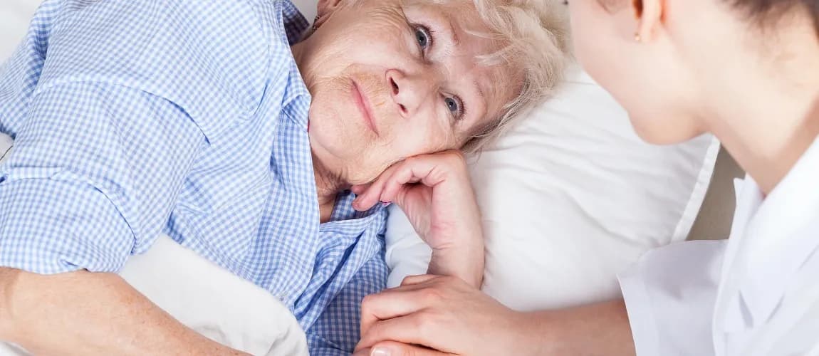 Es ist eine ältere Frau zu sehen, die von einer Pflegerin betreut wird.