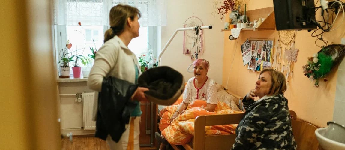 Eine Pflegefachkraft steht in einem Schlafzimmer und unterhält sich mit zwei anderen Frauen.