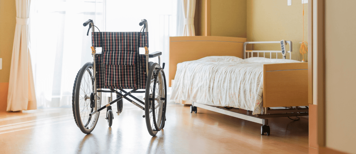 Pflegeheimzimmer mit Rollstuhl und Pflegebett.