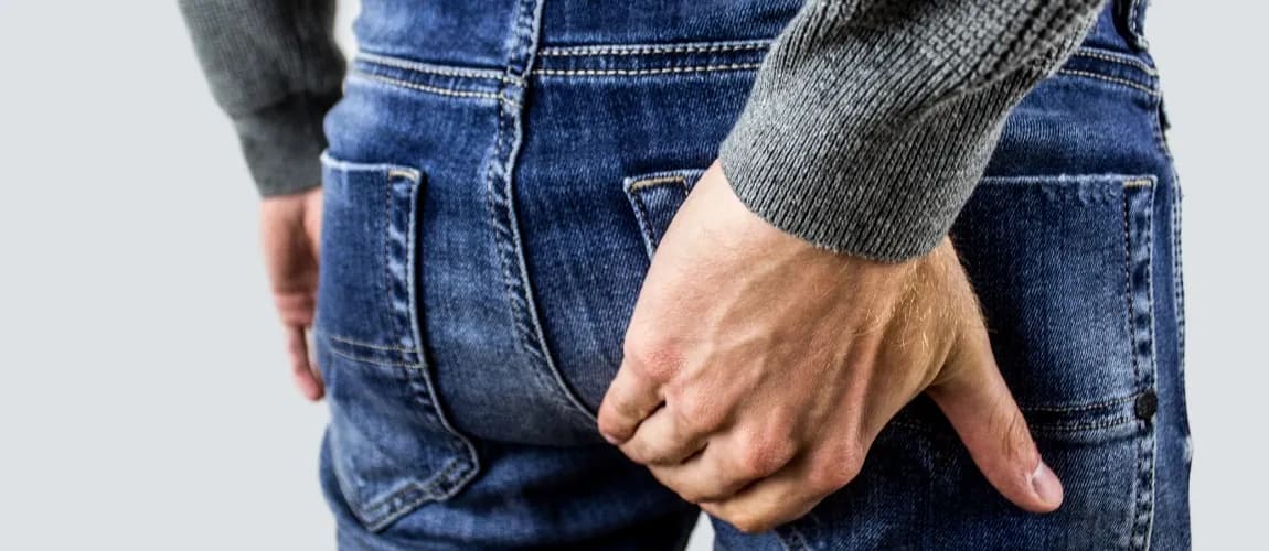 Ein Mann mit Jeans fasst sich an das Gesäß.