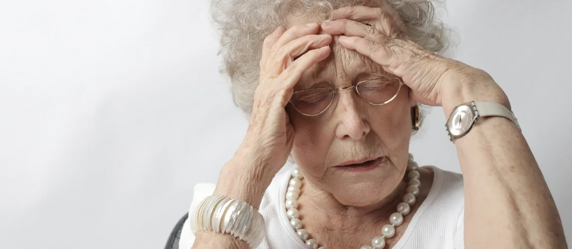 Eine Seniorin hält sich die Hände gegen die Stirn.
