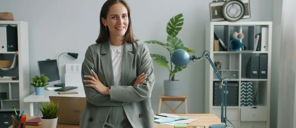 Eine Frau steht mit verschränkten Armen lächelnd im Büro.