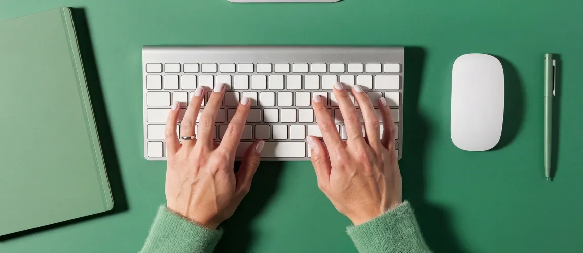 Eine Frau hat beide Hände auf der Tastatur, auf dem Tisch gibt es viele grüne Details.