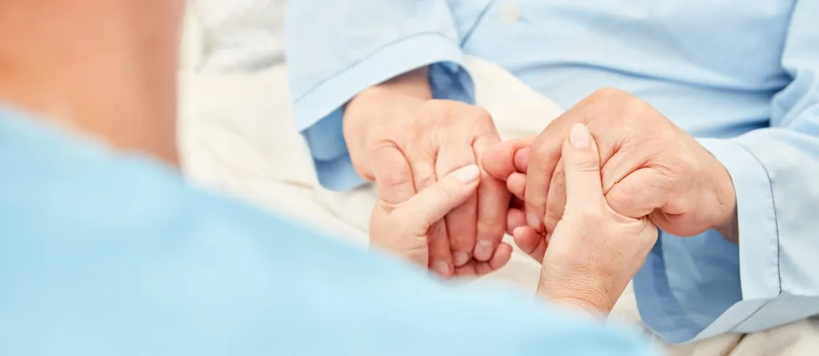 Eine Pflegekraft hält die Hände eines Patienten.