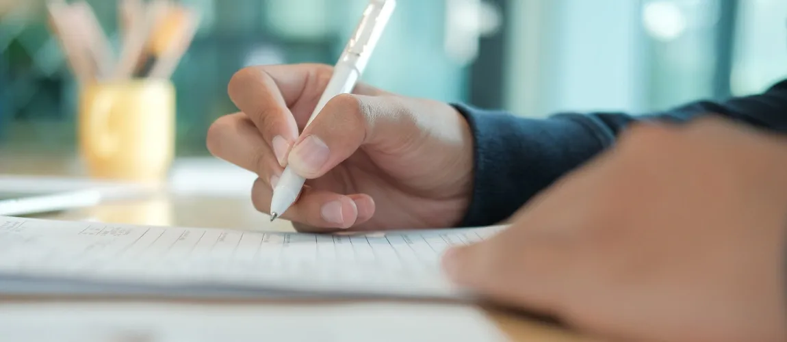 Jemand schreibt eine Bewerbung mit einem Stift auf Papier.