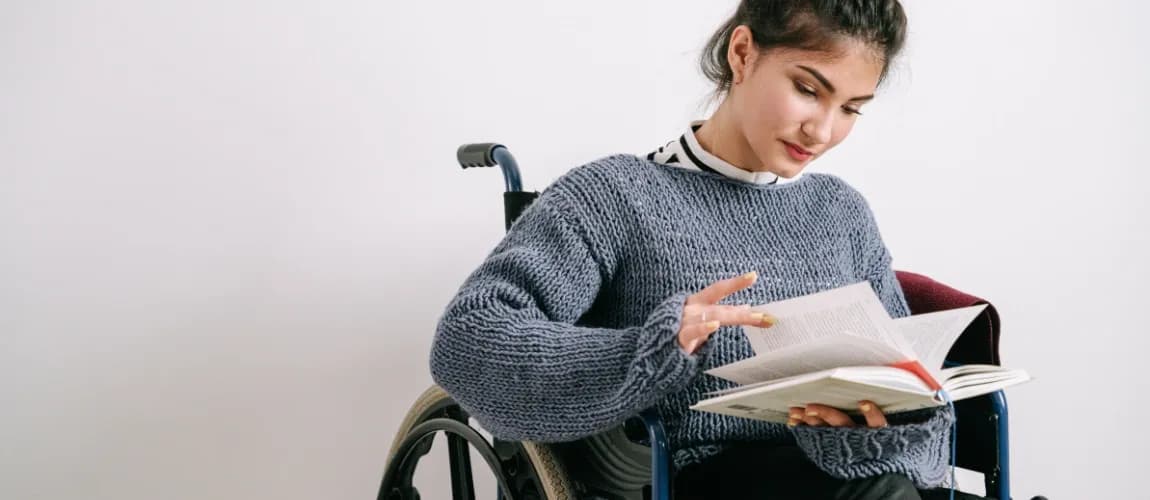 Eine Frau sitzt im Rollstuhl und liest ein Buch.