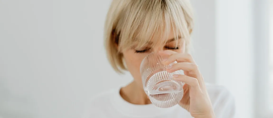 Eine Frau mit blonden Haaren trinkt aus einem Glas Wasser.