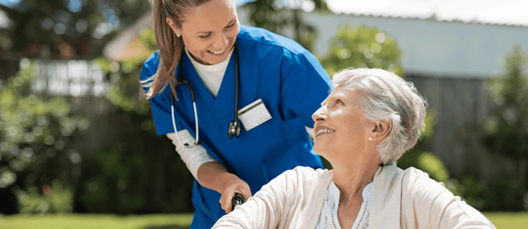 Betreuungskraft schiebt Patientin in Rollstuhl