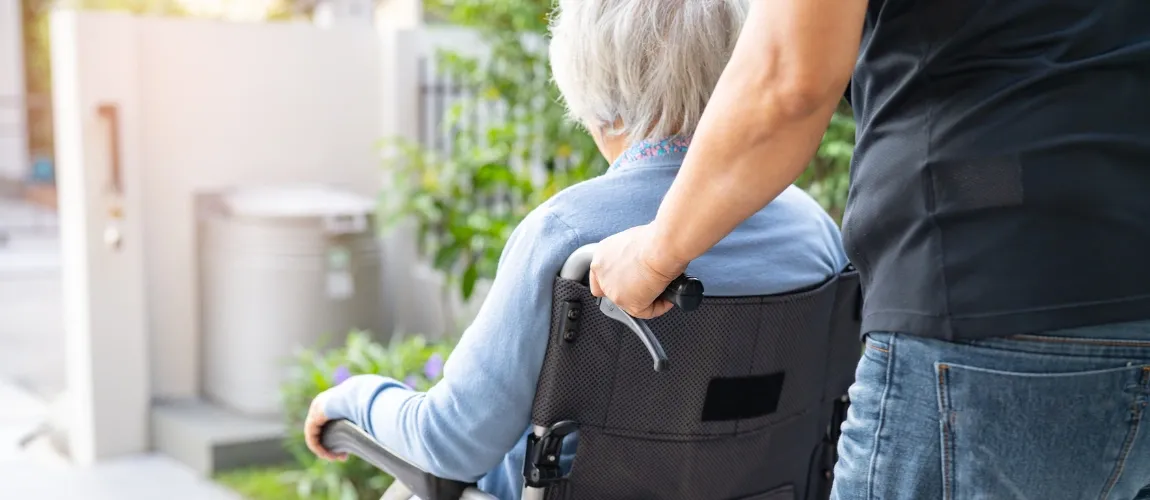 Mann fährt Seniorin in einem Rollstuhl nach draußen