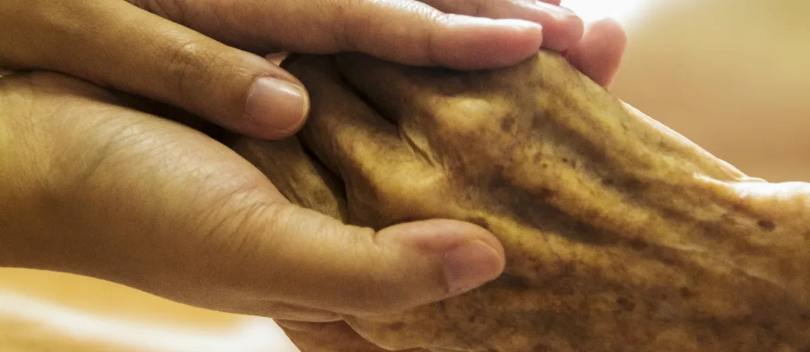 Eine jüngere Hand hält sanft eine ältere Hand.