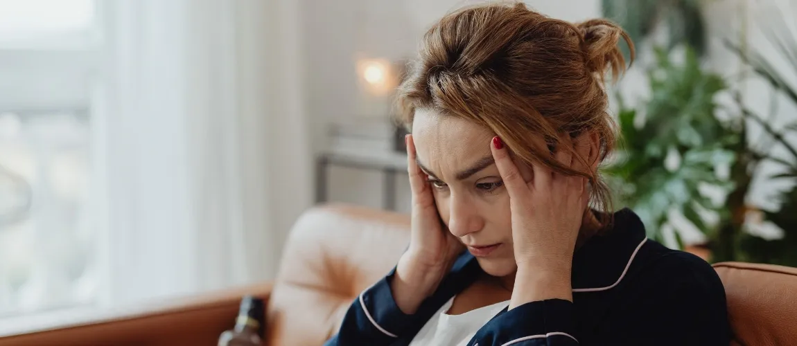 Eine gestresst wirkende Frau sitzt auf dem Sofa und hält sich mit beiden Händen den Kopf.