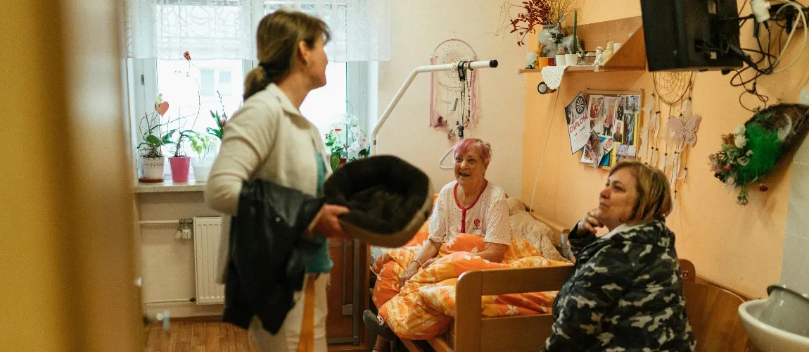 Eine Pflegefachkraft steht in einem Schlafzimmer und unterhält sich mit zwei anderen Frauen.