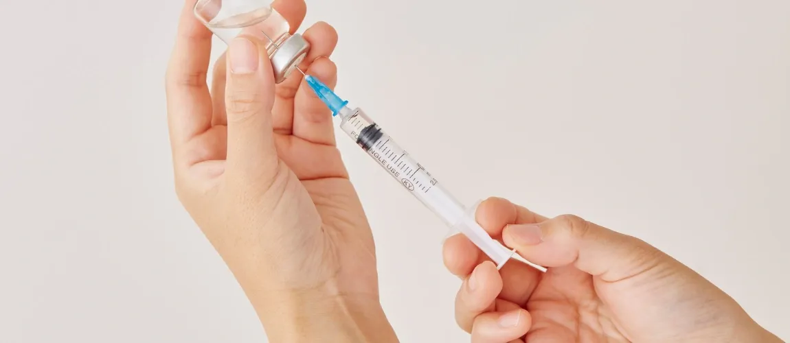 Eine Person zieht eine Spritze mit einem Impfstoff auf.