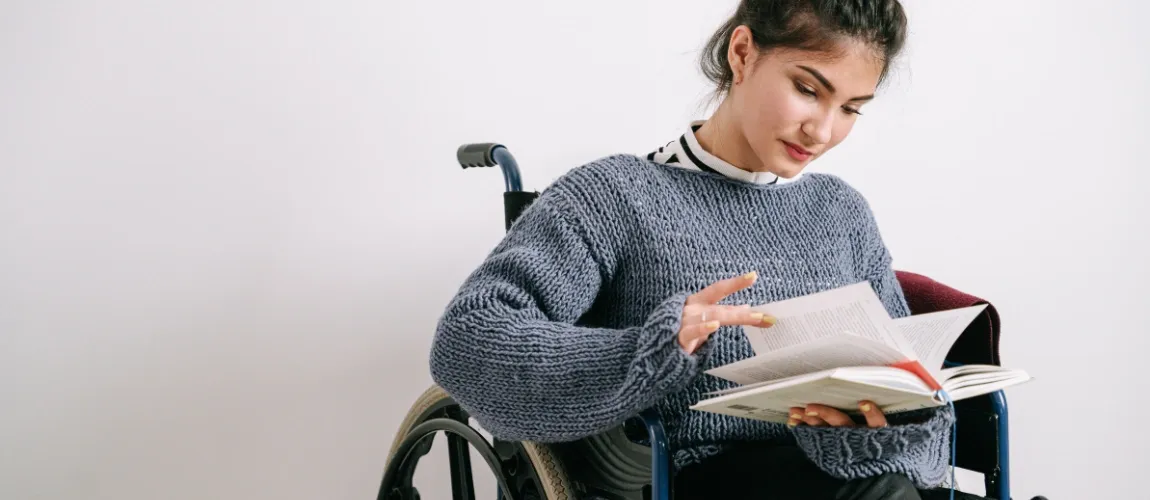 Eine Frau sitzt im Rollstuhl und liest ein Buch. 