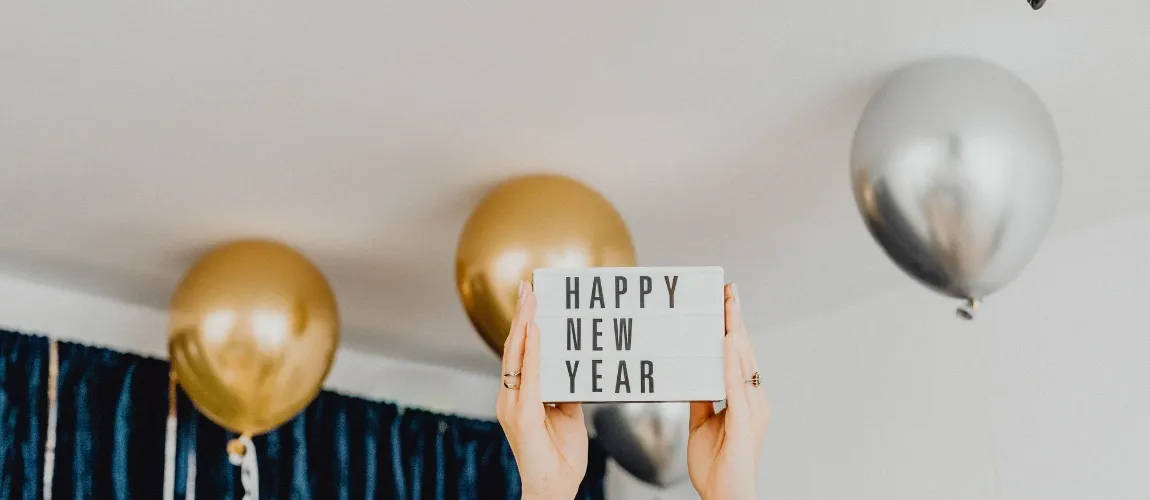 Luftballons "hängen" unter der Decke, ein Schild mit Neujahrsgrüßen wird in die Luft gehalten.