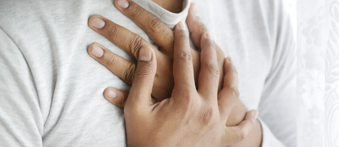 Ein Mann in einem hellen Oberteil hält beide Hände auf die Brust. 