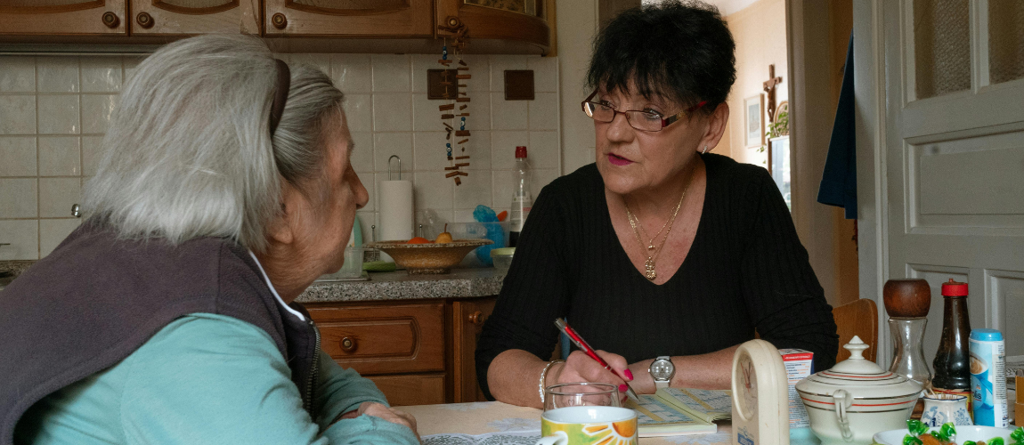 Eine Frau sitzt einer Seniorin in der Küche gegenüber.