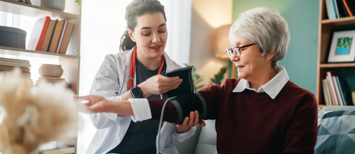Eine Frau misst bei einer Seniorin den Blutdruck.