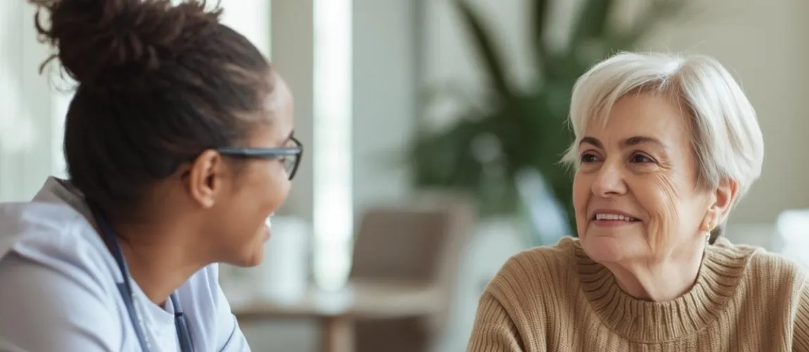 Eine Pflegefachkraft spricht mit einer älteren Frau, beide lächeln.