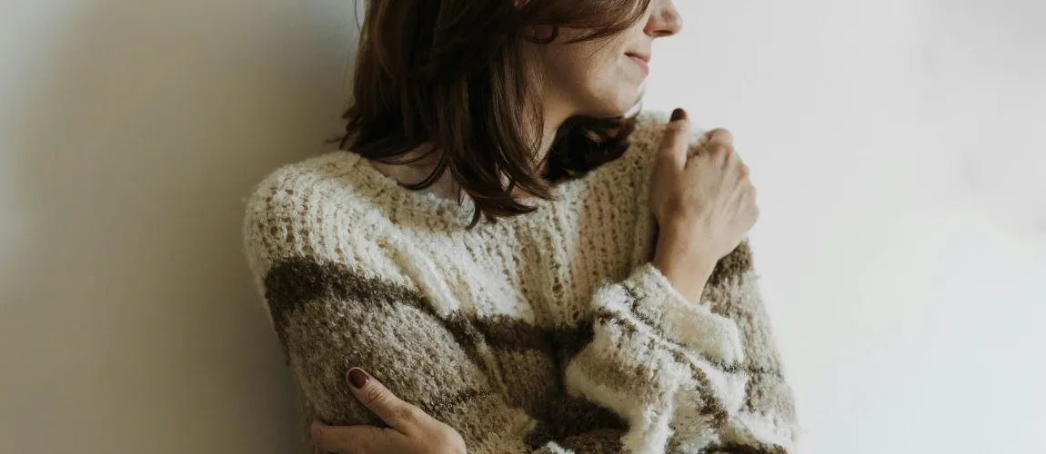 Eine Frau in einem gestreiften Pullover legt die Arme um sich.