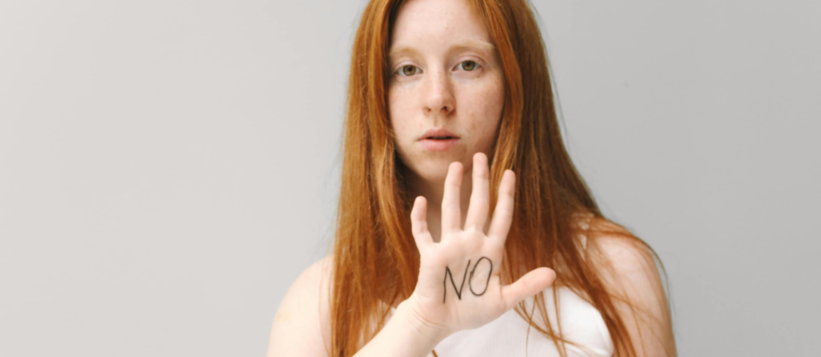 Eine rothaarige Frau hält die Hand die Kamera, darauf steht "NO" geschrieben.